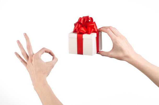 A téma az ünnepségek és ajándékok: kezében egy ajándék csomagolva fehér doboz piros szalag és az íj, a legszebb ajándék elszigetelt fehér background stúdióban - Fotó, kép
