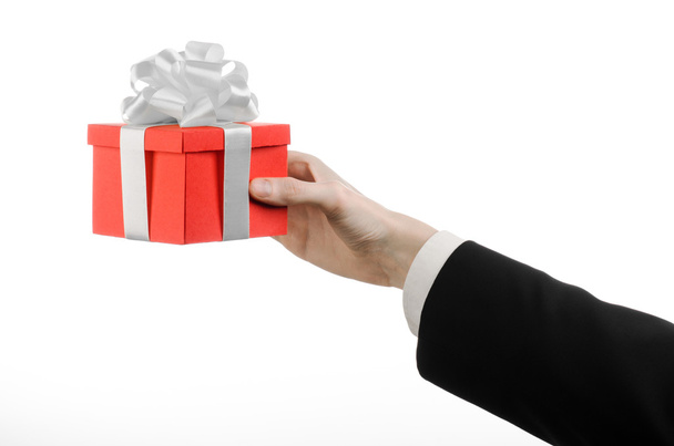 The theme of celebrations and gifts: a man in a black suit holding a exclusive gift wrapped in red box with white ribbon and bow, the most beautiful gift isolated on white background in studio - Photo, image