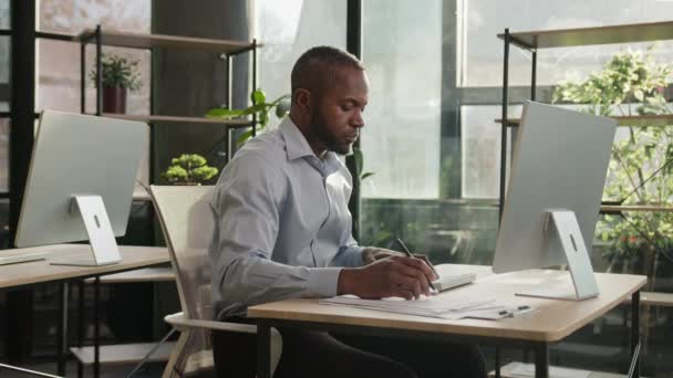 アフリカ系アメリカ人成熟したシニアビジネスマン40sエスニック男性は,オフィスの机に座って中年銀行家マネージャーは,ローン請求書を数える紙にテキストを書くビジネス文書をコンピュータで入力します - 映像、動画