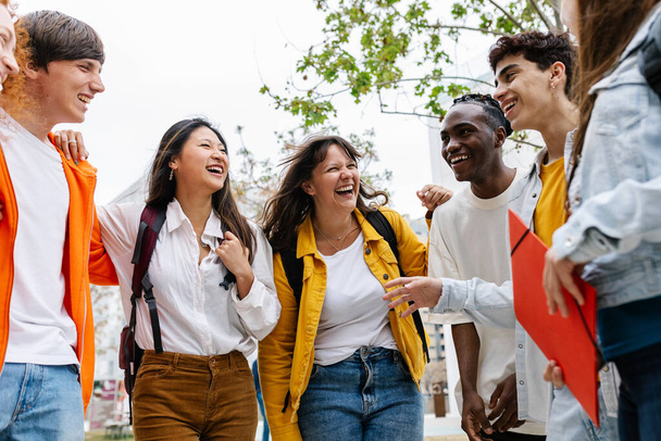 Group of young multi-ethnic students laughing and smiling standing in circle together embraced in the campus of the university. Student life and diversity - Photo, Image