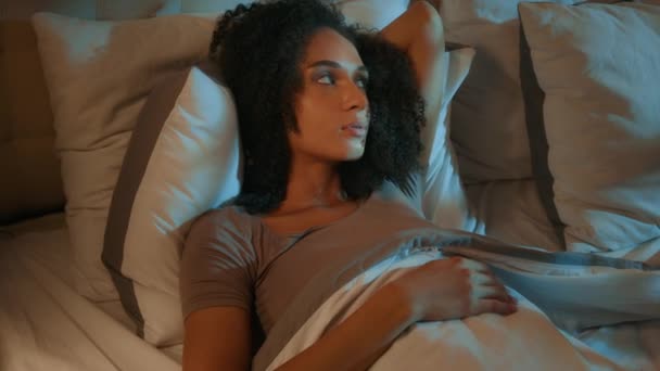 Порушена роздратована афроамериканська молода жінка намагається спати в нічній спальні безсоння прокидається в незручній постільній подушці матрац роздратована дівчина страждає безсонням погані сни проблема сну - Кадри, відео