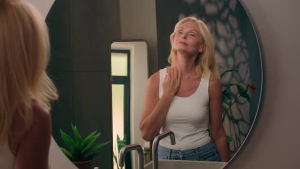 Valkoihoinen vanha vanhempi kypsä nainen katselee peiliä kotona kylpyhuone touch kasvot ja kaula tarkistaa jäljitellä ryppyjä kehon venytys markkaa ihon ikääntyminen ihonhoito anti-aging kauneudenhoitotuotteet nuorentaminen - Materiaali, video