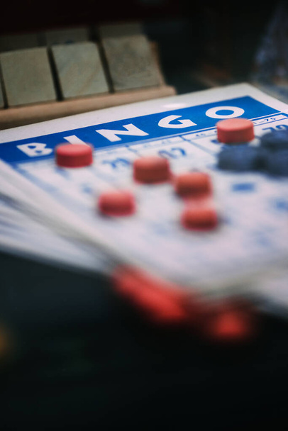 Dit beeld vangt de sensatie van een bingo spel in uitvoering, met de nadruk op een close-up weergave van een kaart met nummers bedekt door rode markeringen. - Foto, afbeelding