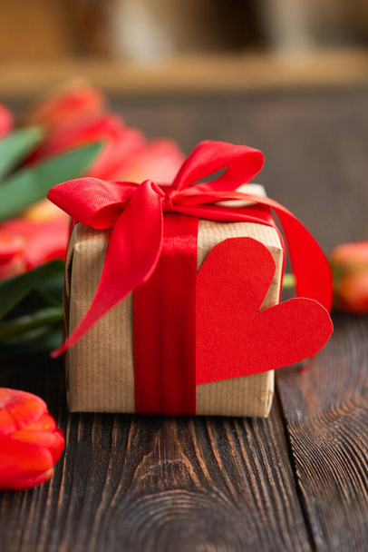 Bouquet of beautiful fresh orange tulips with gift boxe and red paper hearts on wood background. Greeting card with copy space for Valentines Day, Womans Day and Mothers Day. - Photo, Image