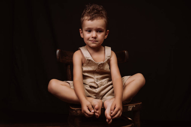 upset sad boy crying sitting on a wooden chair on a dark background - Photo, Image
