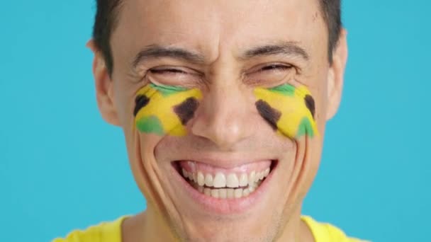 Відео в студії з хромою крупним планом чоловіка з ямайським прапором, намальованим на обличчі, посміхаючись на камеру - Кадри, відео