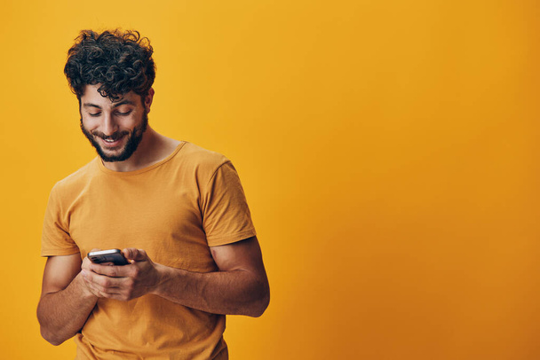 Retrato hombre sosteniendo teléfono negocio joven tecnología modelo chico mensaje alegre comunicación amarillo sonrisa fondo persona móvil adulto teléfono inteligente guapo internet en línea chat feliz - Foto, imagen