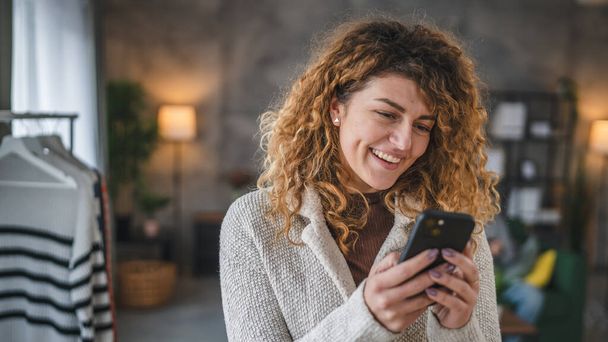 Egy nő kaukázusi felnőtt nő göndör haj otthon használata mobiltelefon okostelefon sms SMS-ezés vagy böngészés internet online közösségi hálózat - Fotó, kép