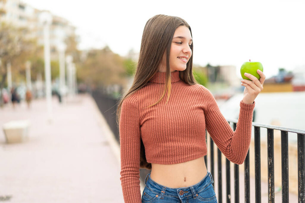 Teenager Mädchen mit einem Apfel im Freien mit glücklichem Gesichtsausdruck - Foto, Bild