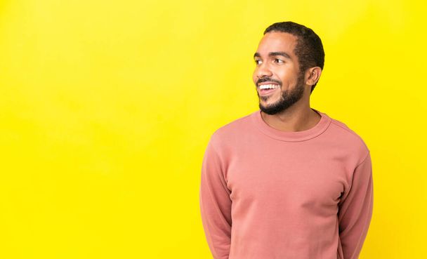 Young latin man isolated on yellow background looking to the side and smiling - Fotoğraf, Görsel