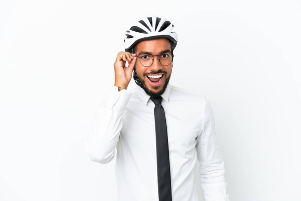 Young business latin man holding a bike helmet isolated on white background with glasses and surprised - Photo, Image