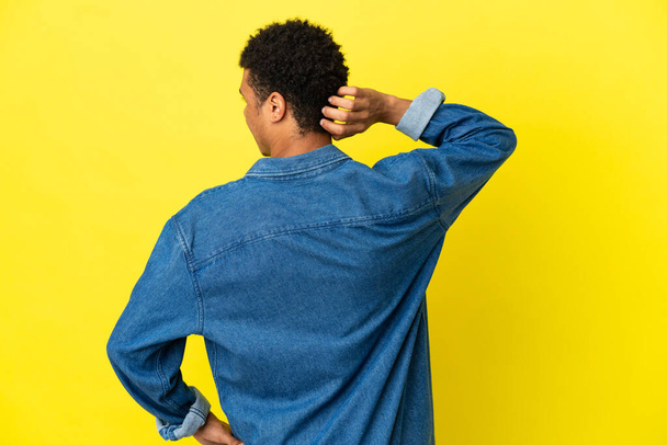 Joven hombre afroamericano aislado sobre fondo amarillo en la espalda posición y pensamiento - Foto, imagen