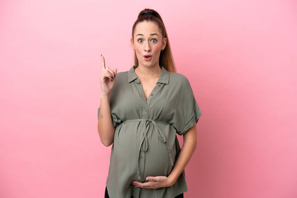 Νεαρή γυναίκα απομονωμένη σε ροζ φόντο έγκυος και σκέφτεται - Φωτογραφία, εικόνα