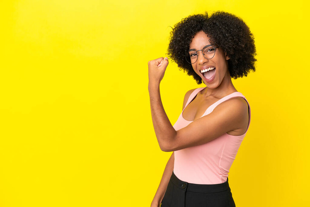 黄色の背景に孤立した若いアフリカ系アメリカ人女性が勝利を祝う - 写真・画像