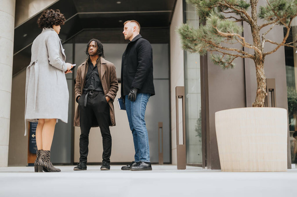 Tres colegas de negocios multiculturales en una reunión informal fuera de un edificio de oficinas. Compromiso y asociación en un entorno urbano. - Foto, Imagen