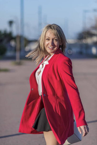 Una donna bionda in giacca rossa in piedi e in posa per strada - Foto, immagini