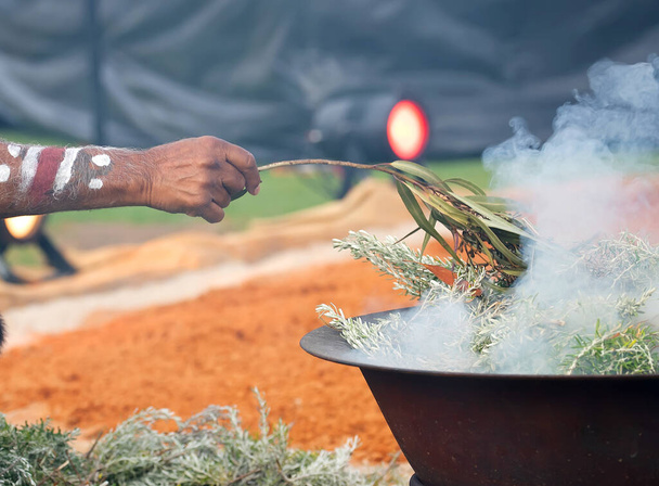 Mano humana con rama verde de eucalipto, humo y fuego, rito ritual de humo en un evento comunitario indígena en Australia - Foto, imagen