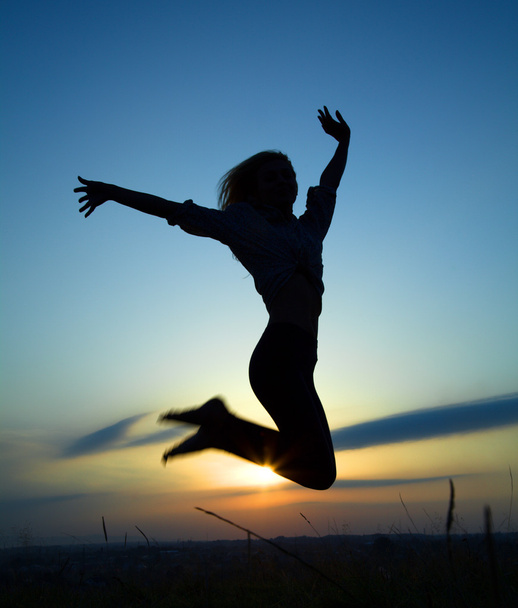Silhouette of a girl jumping over sunset - Foto, imagen
