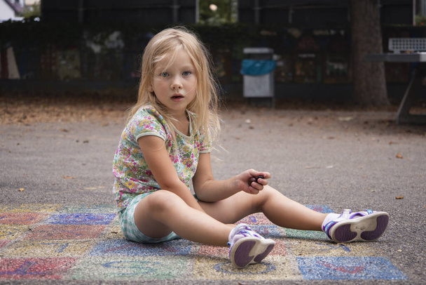Child girl blonde preschool age is played sitting on the pavement. - Foto, imagen