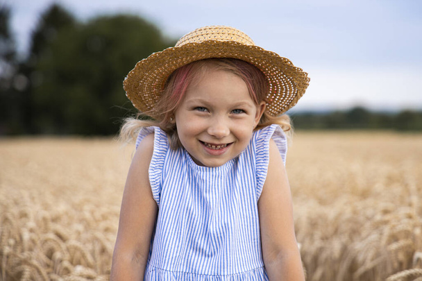 Χαμογελαστό ξανθό κορίτσι που φοράει καπέλο σε χωράφι με σιτάρι. - Φωτογραφία, εικόνα