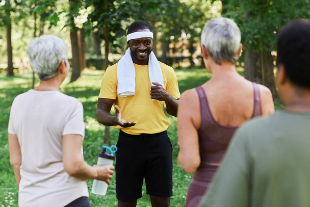 Portrait of smiling trainer talking to diverse group of senior women during outdoor sports workout - Photo, Image