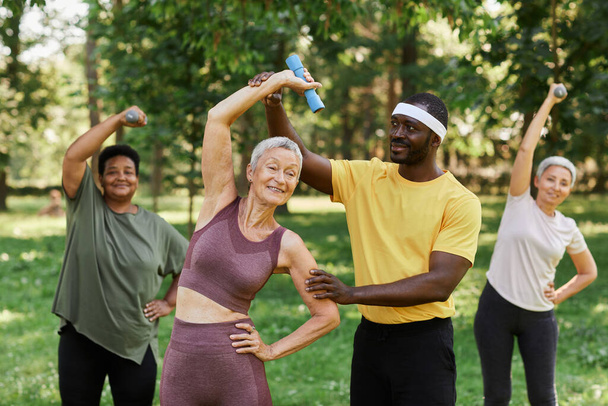 Pas w górę portret męski trener sportowy pomagając starszej kobiecie korzystających z treningu sportowego na świeżym powietrzu w parku - Zdjęcie, obraz