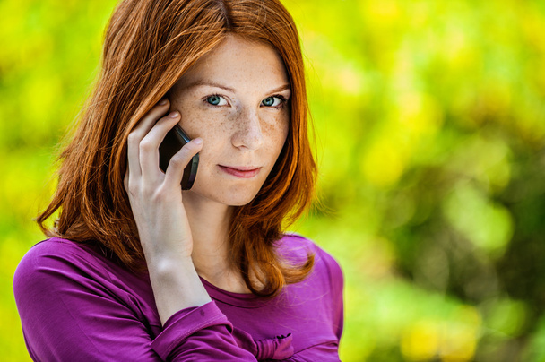 κοκκινομάλλης χαμογελώντας νεαρή γυναίκα μιλάει στο τηλέφωνο - Φωτογραφία, εικόνα