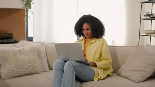 Focalisé afro-américaine fille pigiste ethnique femme travaillant avec ordinateur portable sur le canapé jeune étudiant e-learning étude à distance shopper femme d'affaires shopping en ligne à la maison appartement - Séquence, vidéo