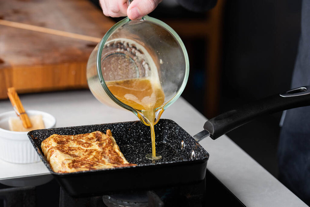 Chef homme mains cuisson Tamagoyaki ou Tamago traditionnelle japonaise Omelette roulée recette, faite en roulant plusieurs couches d'œufs brouillés cuits fouetter dans une casserole dans une omelette rectangulaire. - Photo, image