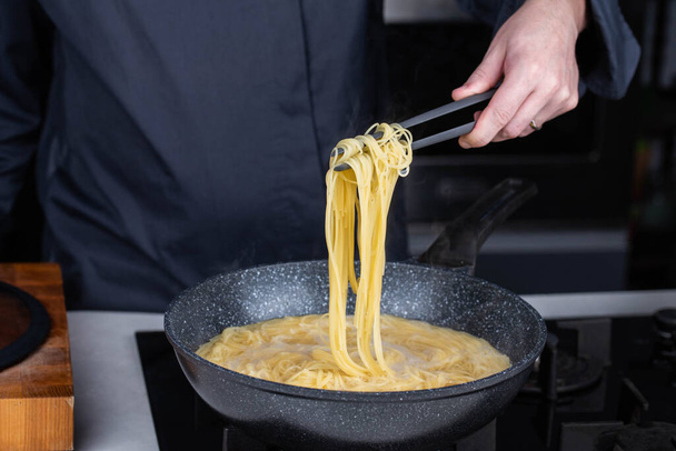 Professionele chef koks maken Italiaanse Capellini spaghetti pasta bij moderne keuken gasfornuis in wok pan pot in kokend water. Stoom uit heet voedsel. - Foto, afbeelding