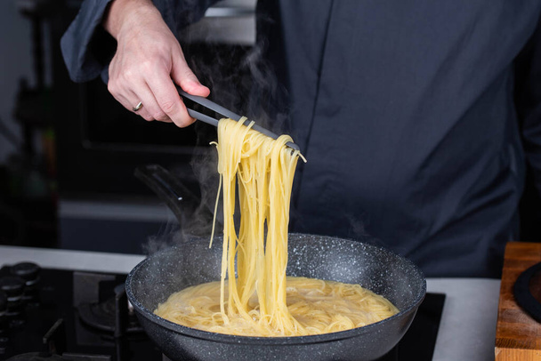 Professioneller Koch kocht italienische Capellini-Spaghetti am modernen Gasherd in einem Wok-Topf mit kochendem Wasser. Dampf aus heißem Essen. - Foto, Bild