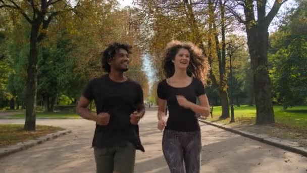 Щасливі багаторасові бігуни здоровий спортсмен і спортсмен, бігають на вулиці тренування разом фітнес-пара сміється біг спортивна активність Аравійський чоловік і кавказька жінка біг біг в осінньому міському парку - Кадри, відео