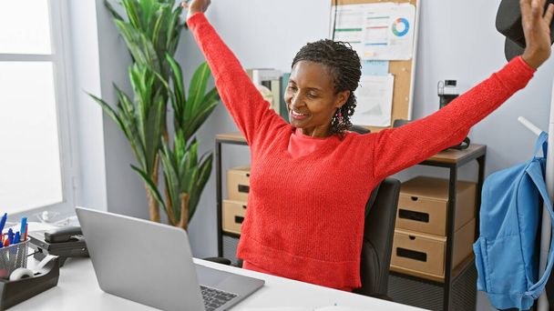 Eine fröhliche afrikanisch-amerikanische Frau dehnt sich in einem modernen Büroumfeld und stellt das Wohlbefinden am Arbeitsplatz dar. - Foto, Bild