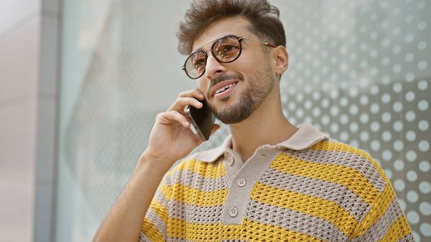 Hombre árabe joven sonriendo confiado hablando en el teléfono inteligente en la calle - Foto, imagen