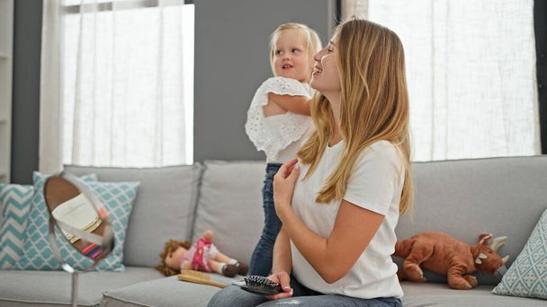 Confident caucasian mother sits comfortably, combing daughter's hair on sofa - heartwarming family scene at home - Photo, Image