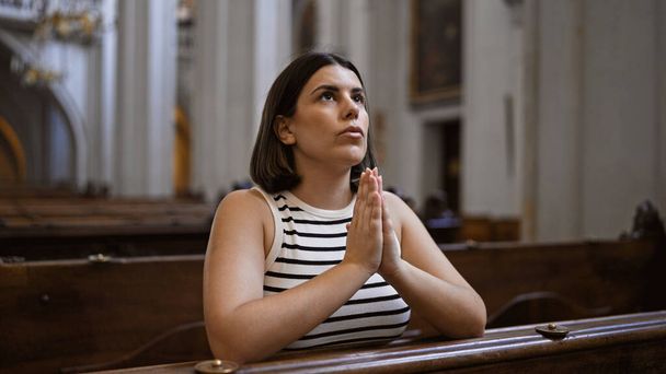 Jovem mulher hispânica bonita orando em um banco de igreja na Igreja Agostiniana em Viena - Foto, Imagem