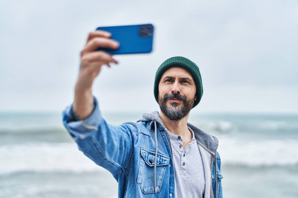 Νέοι φαλακρός άνθρωπος χαμογελά αυτοπεποίθηση κάνοντας selfie από το smartphone στην παραλία - Φωτογραφία, εικόνα