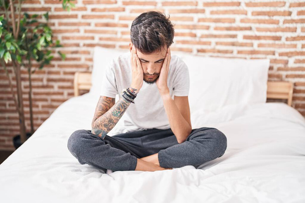 Giovane uomo ispanico stressato seduto sul letto in camera da letto - Foto, immagini