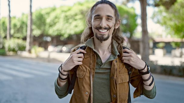 Молодой латиноамериканец в рюкзаке улыбается в парке - Фото, изображение