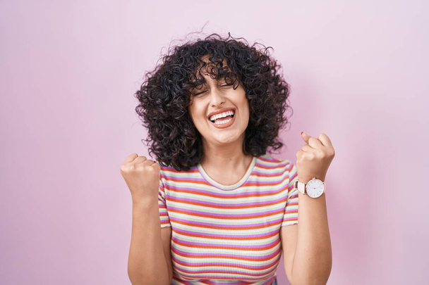 Jovem mulher do Oriente Médio em pé sobre fundo rosa muito feliz e animado fazendo gesto vencedor com os braços levantados, sorrindo e gritando para o sucesso. conceito de celebração.  - Foto, Imagem