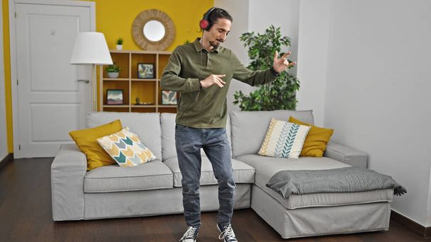 Nuori latino mies hymyilee luottavainen kuunnella musiikkia tanssia kotona - Valokuva, kuva
