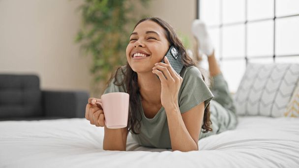 Африканская американка разговаривает по смартфону, пьет кофе в спальне - Фото, изображение