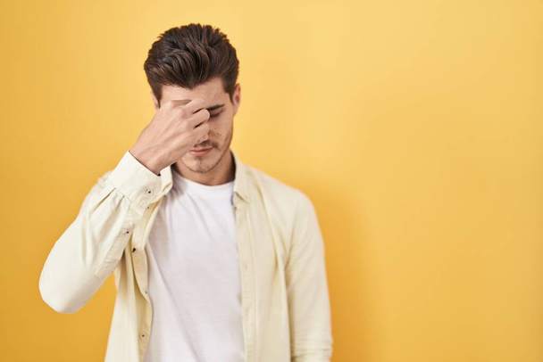 Jeune homme hispanique debout sur fond jaune fatigué se frottant le nez et les yeux ressentant fatigue et maux de tête. concept de stress et de frustration.  - Photo, image
