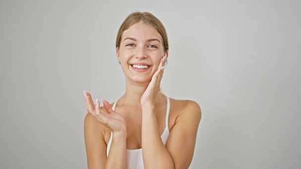 Jeune femme blonde souriante confiante toucher le visage sur fond blanc isolé - Photo, image