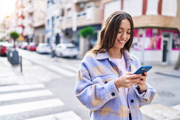 Joven hermosa mujer hispana sonriendo confiada usando teléfono inteligente en la calle - Foto, imagen
