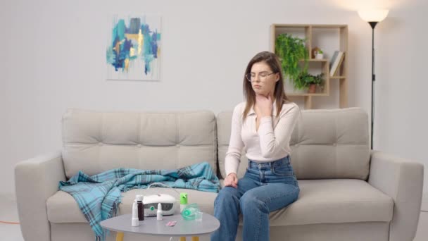 Jonge vrouw met keelspray zittend op de bank thuis - Video