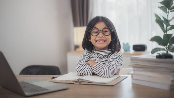 Ευτυχισμένος μαθητής κοριτσάκι σπουδές σε απευθείας σύνδεση χρησιμοποιώντας ένα φορητό υπολογιστή στο σπίτι, χαμογελώντας μικρό παιδί προτείνουμε τάξη ή μάθημα. - Φωτογραφία, εικόνα