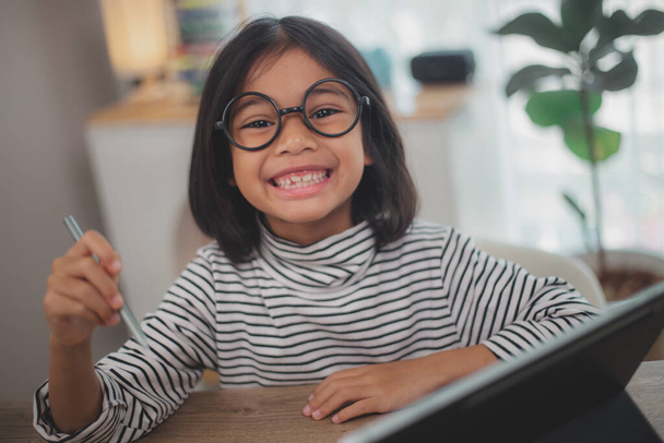 Onnellinen pieni tyttö oppilas opiskelee verkossa kannettavan tietokoneen avulla kotona, hymyilevä pieni lapsi suosittelee luokkaa tai oppituntia. - Valokuva, kuva