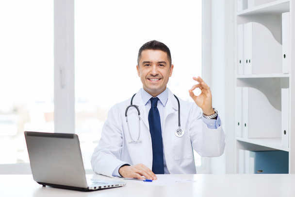 smiling doctor with laptop showing ok in office - Fotó, kép