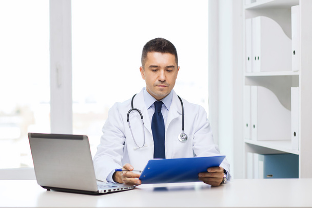 male doctor with clipboard and laptop in office - Fotó, kép